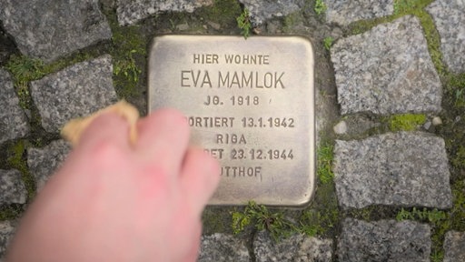 Ein im Straßenpflaster eingelassener Stolperstein wird mit einem Lappen poliert