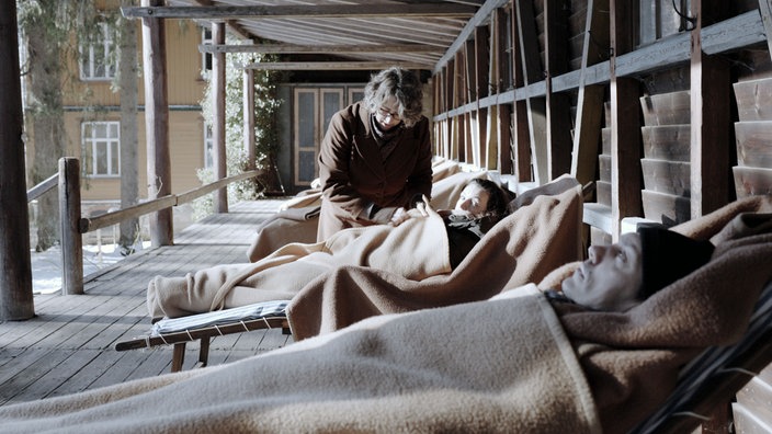Filmstill aus dem Film "Formen moderner Erschöpfung". Drei Menschen auf der Terrasse eines Sanatoriums
