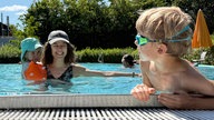 Eine Frau schwimmt mit zwei kleinen Kindern in einem Freibadbecken in Köln-Zündorf