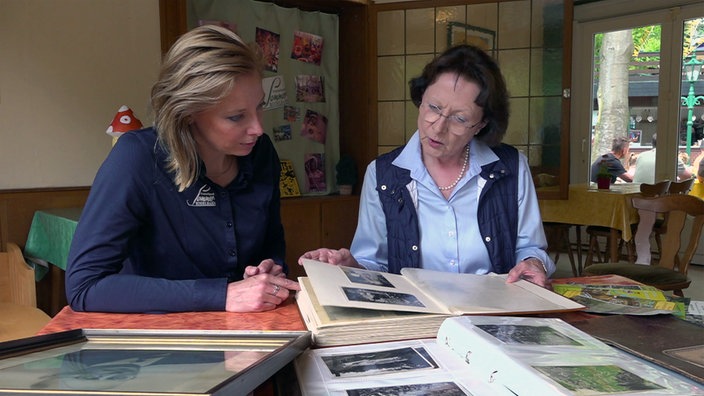 Zwei Frauen sitzen an einem Tisch und blättern alte Fotoalben durch 