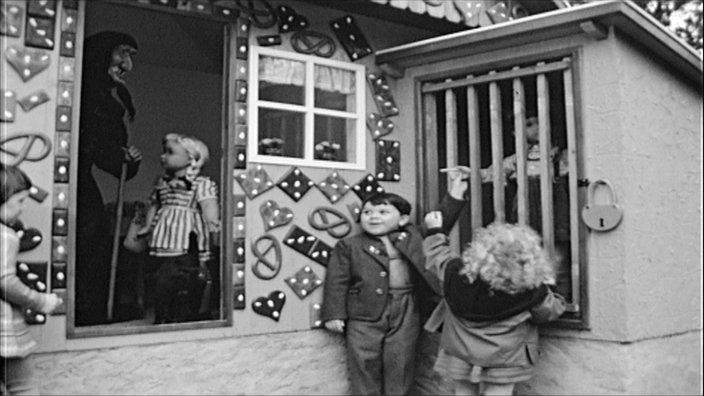 Eine schwarz-weiß Aufnahme zeigt Kinder vor einem Märchenhaus