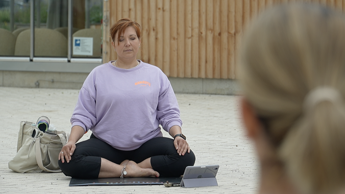Teilnehmerin schaut auf Yoga-Lehrerin im Schneidersitz auf ihrer Matte