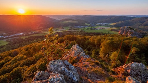 Die Sonne geht über dem Rothaargebirge unter, im Vordergrund sieht man die Bruchhauser Steine, wie sie in orangenes-gelbes Licht getaucht werden
