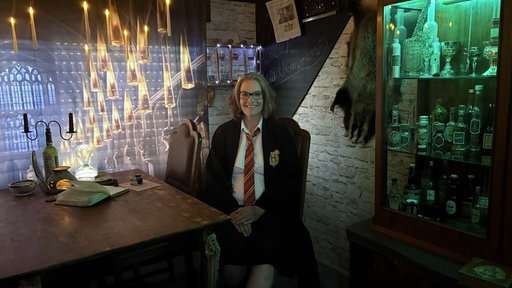 Ilona Balon sitzt in einem Harry-Potter-Outfit an einem Tisch in der Großen Halle