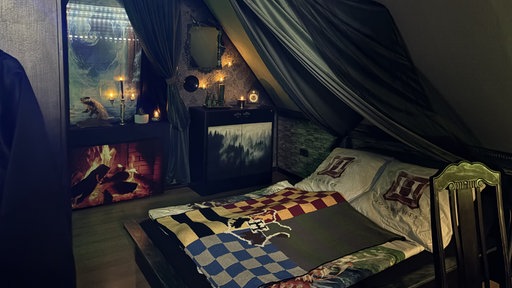 Ein dunkles Zimmer mit Bett auf dem das Slytherin-Wappen ist.