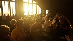 Viele Menschen häkeln für das Rekordmammut, dabei sitzen sie zwischen der Industierkultur des Ruhr Museums auf Zollverein, die Lichtstimmung ist ganz warm, weil die letzten Sonnenstrahlen in die Fenster scheinen.