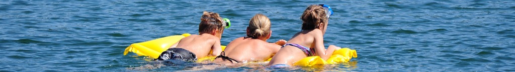 Drei Schwimmer auf einer Luftmatratze im Wasser