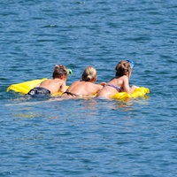 Drei Schwimmer auf einer Luftmatratze im Wasser