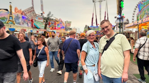 Claudia und Leo Becker stehen zwischen vielen Menschen und Buden mitten auf der Cranger Kirmes.