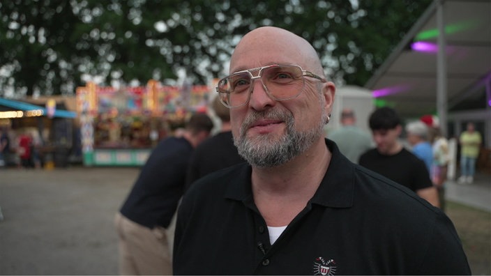 Ein Mann auf einem Volksfest schaut lächelnd in die Kamera 
