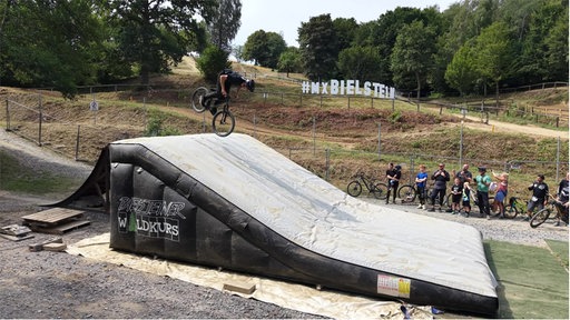 Mountainbiker springt über Rampe und landet auf einem riesigen Luftkissen