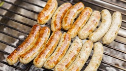 Das Bild zeigt Bratwürstchen auf einem Grill.