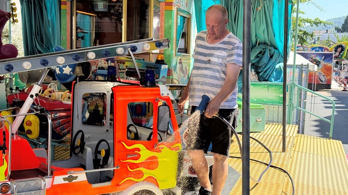 Ein Mann spritzt mit einem Schlauch ein Feuerwehrauto in einem Kinderkarussell ab.