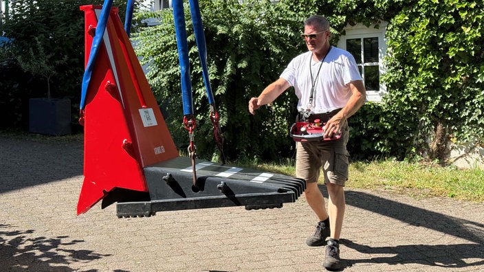 Ein Mann steuert mit einer Art Controller, der um seinen Hals hängt, eine Fixierung einer großen Metallkonstruktion.