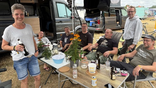 Eine Gruppe sitzt auf einem Campingplatz um einen Tisch herum.
