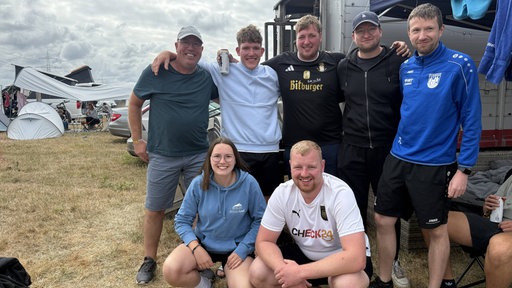 Eine Gruppe junger Menschen steht Arm in Arm auf einer Wiese