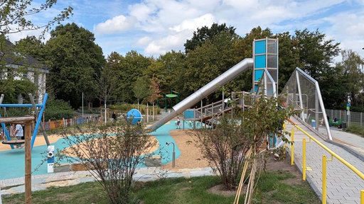 Ein Spielplatz mit großen blauen und beigen Spielgeräten umgeben von Bäumen