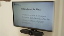 Auf dem Bild sieht man einen Bildschirm sowie eine Kamera, der Bildschirm zeigt an Patienten gerichtete Anweisungen. 