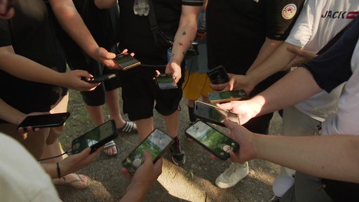 Pokemon GO-Spieler stehen im Kreis und und halten ihre Handys in die Runde. Auf dem Bildschirm ist das Spiel geöffnet. 