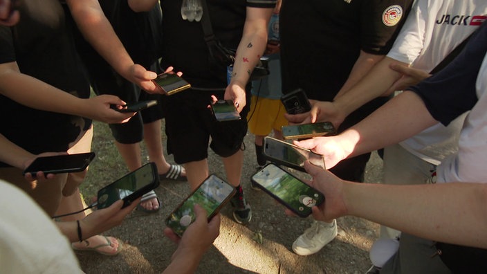 Pokemon GO-Spieler stehen im Kreis und und halten ihre Handys in die Runde. Auf dem Bildschirm ist das Spiel geöffnet. 