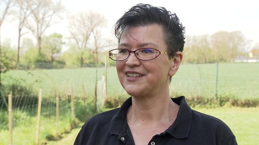 Frau mit Brille und kurzen schwarzen Haaren lächelt leicht.