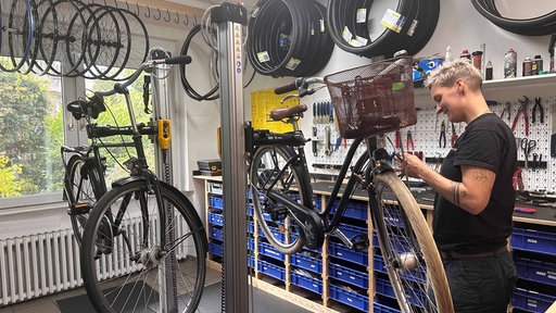 Eine Zweiradmechanikerin schraubt an einem Rad.