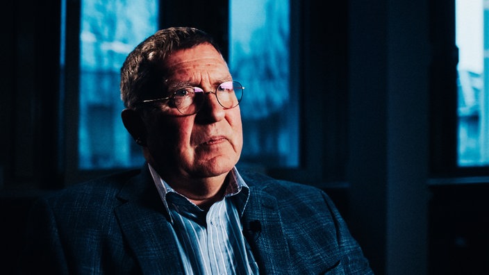 Rainer Becker im Portrait in einem abgedunkelten Raum.