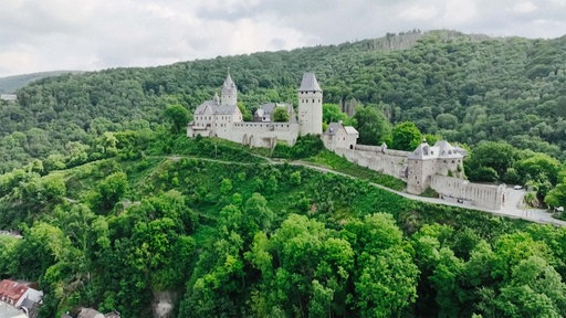 Burg Altena im Sommer vor grün bewaldeten Hügeln.