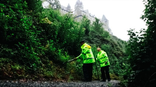 Zwei Polizisten in gelber Warnweste suchen bei Burg Altena nach Spuren.