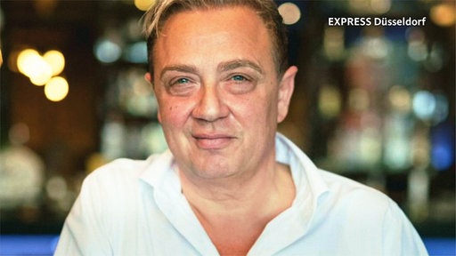 Santo Sabatino, ein brünetter Mann mit Seitenscheitel, glattem Gesicht und blauen Augen, schaut in die Kamera und lächelt.