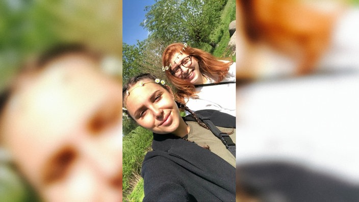 Saskia und Derya stehen in einem Park auf einer Wiese. Beide tragen einen selbsgeflochtenen Blumenkranz in den Haaren.