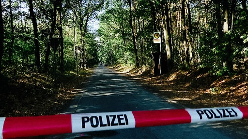 Ein Absperrband an einer Straße in einem Waldgebiet.