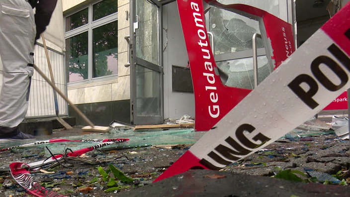 Glasscherben vor einem Geschäftsgebäude, ein Mann kehrt vor dem Eingang
