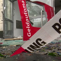 Glasscherben vor einem Geschäftsgebäude, ein Mann kehrt vor dem Eingang