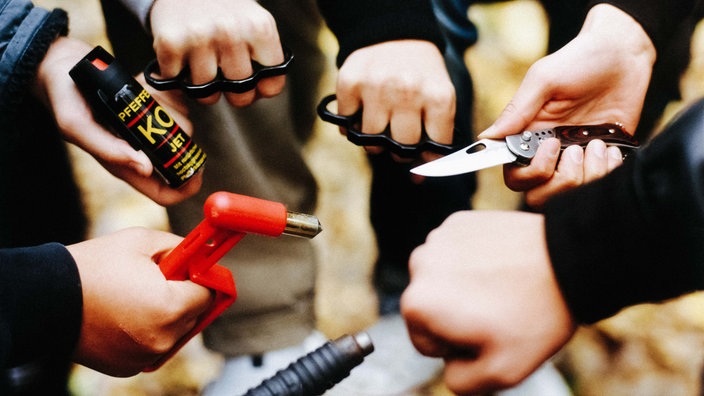 Kinder halten Schlagringe, Messer und Pfefferspray in den Händen.