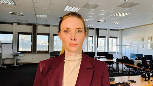 Staatsanwältin Miriam Polk in einem Konferenzraum. Sie trägt einen roten Blazer 