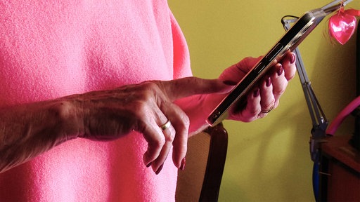 Eine Frau hält ein Handy in ihrer linken Hand. Mit der rechten Hand scrollt sie auf dem Bildschirm.