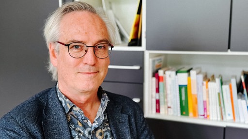 Christoph Grotepass mit Brille und kurzen gräulichen Haaren. Im Hintergrund ein Bücherregal