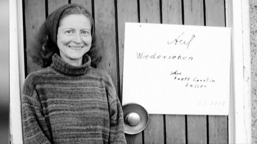 Anett Carolin Kaiser steht neben inem Schild, auf dem "Auf Wiedersehen, Ihre Anett Carolin Kaiser" steht.