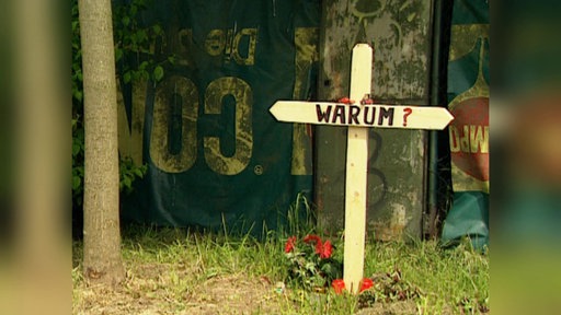 Archiv-Bild: Auf einer Grünfläche steht ein Kreuz aus Holz. Darauf steht in großer Schrift "WARUM?"