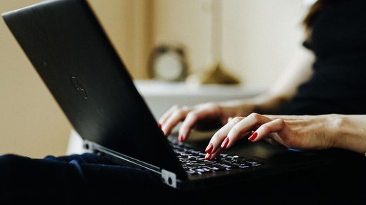 Hände, die auf der Tastatur eines Laptops tippen.