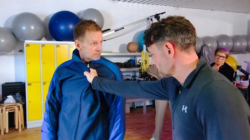 Trainer Dirk Eisenblätter gegenüber einem Mann. Dieser hält seine Faust an den Kragen von Dirk.