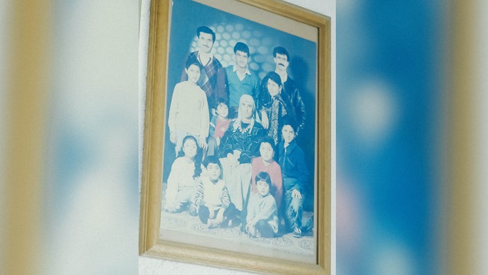 Ein Foto in einem Rahmen, es sind mehrere Erwachsene und Kinder zu sehen. 