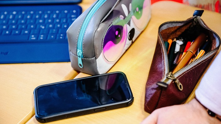 Ein Tisch auf dem zwei Federmappen, ein Laptop und ein Smartphone liegt