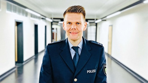 Nahaufnahme von Andreas Reuter in Polizeiuniform. Er lächelt.