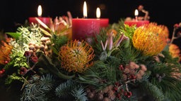 Das Bild zeigt einen Adventskranz mit roten Kerzen.