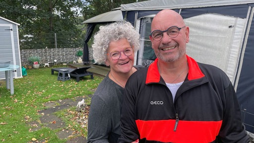 Die Camper Doris Hegemann-Lenz und Matthias Lenz gucken auf ihrem Platz in die Kamera.