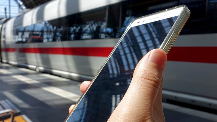 Eine Frau hält ihr Smartphone am Bahnsteig vor einem ICE.