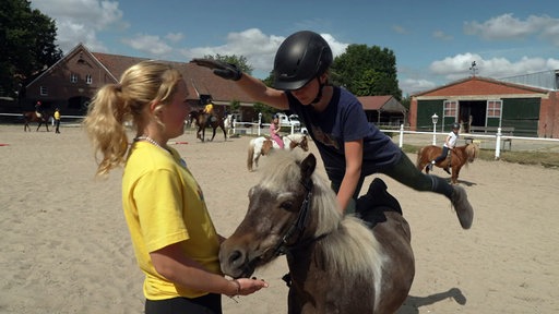 Ein Kind turnt auf einem Pony.