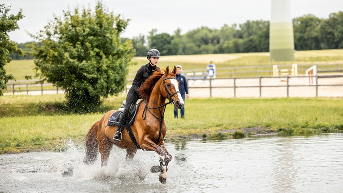 Eine junge Frau reitet mit einem Pferd durch Wasser.